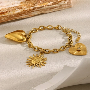 Macro shot of gold plated O-chain bracelet with sun and heart charms on stone base