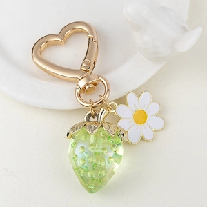 Detail of cute strawberry and daisy keychain with gold heart clasp on a porcelain plate