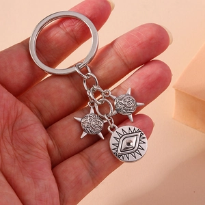 Handheld silver metal keychain featuring creative sun faces and eye charms on beige background
