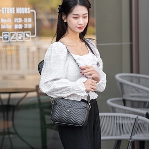 Detail of black V-quilted crossbody bag with gold buckle on a stylish white blouse