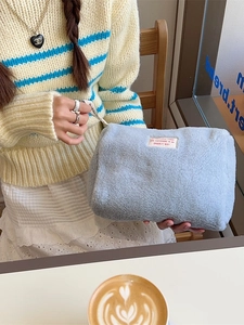 Light blue teddy fleece makeup bag with zipper closure and decorative woven labels