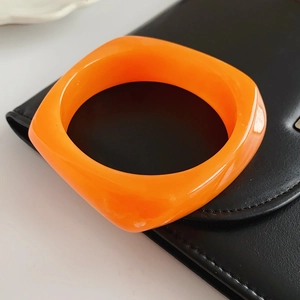 Detail of bright orange resin square bracelet on black leather and white surface