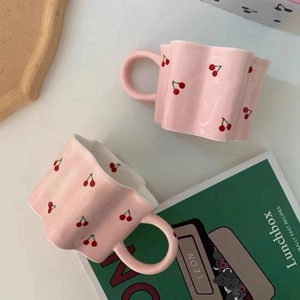 Detalle de la taza de cerámica rosa con patrones de cerezas rojas y borde ondulado