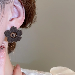 Close-up of a brown velvet floral earring with leopard print bead on a model's ear