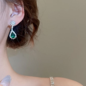 Detail of luxury teardrop earring with green gemstone and pave-set zircons on model