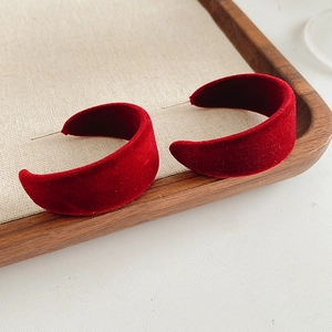 Detail view of red velvet C-shaped hoop earrings on a minimalist wooden tray display