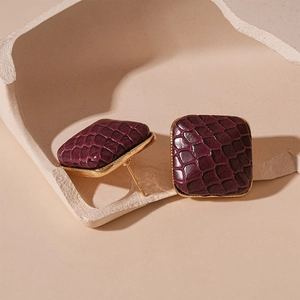 Detail of square purple faux-leather earrings with golden metal edges and sharp texture