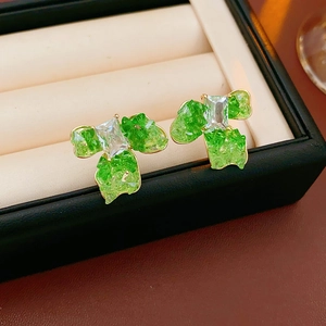 Macro shot of gold-plated flower earrings with green crystals on a beige cushion