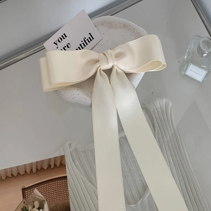Close-up of a large cream satin bow hair clip with long ribbons on a textured surface