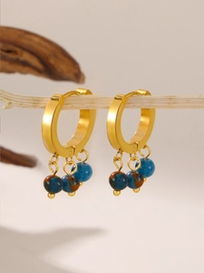 Macro view of gold hoop earrings with marble stone beads on a wooden branch