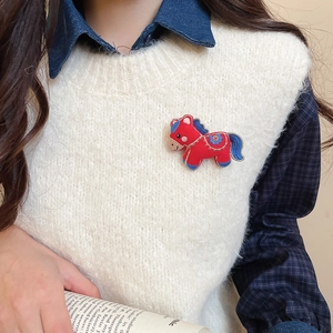 Close-up of a red knitted horse brooch with blue embroidery on a white vest