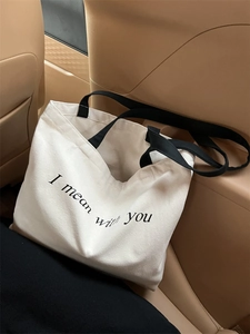 Detail shot of a white canvas tote bag with black slogan on a leather car seat
