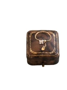 Adjustable gold chain ring with white clover charm and dangling heart on a leather box