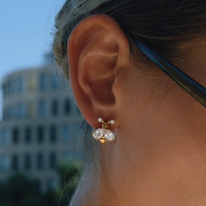 Close-up of a 18K gold-plated bee earring with white zircons worn on a model's ear