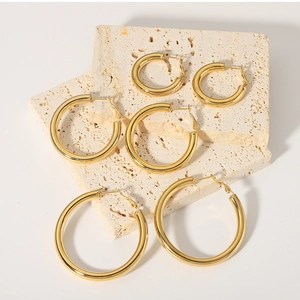 Detailed view of three sizes of gold-plated hollow hoop earrings on a stone base