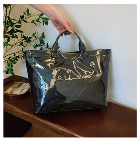 Close-up of black glossy tote bag showing textured patent leather and white TOTE BAG text