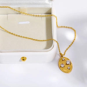 Macro detail of a gold oval pendant set with clear zircons inside a white jewelry box