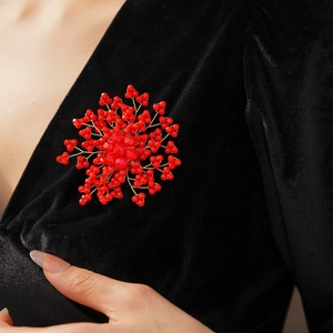 Close-up of a handcrafted red beaded flower brooch with pearls on black velvet fabric