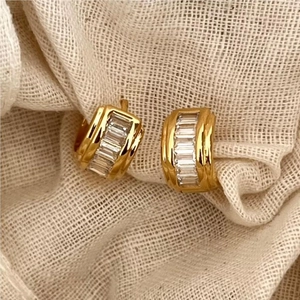 Elegant gold square baguette-cut crystal stud earrings on beige textured fabric