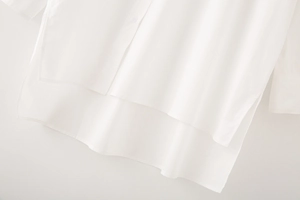 Detail of white cotton shirt featuring irregular high-low hem and side slit craftsmanship