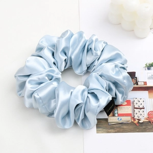 Close-up of light blue satin scrunchie with brand tag next to a decorative candle