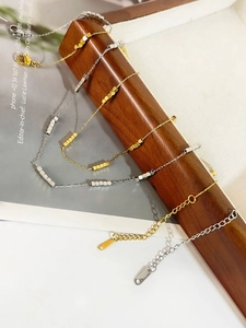 Detail of titanium steel square bead necklaces in gold and silver on a wooden stand