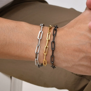 Close-up of three men's stainless steel paperclip chain bracelets in silver, gold, and black