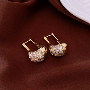 Close-up of gold U-shaped earrings with pavé set white zircons on silk background