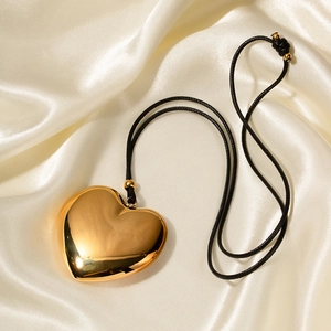 Gros plan du pendentif cœur en or 18k sur cordon noir sur fond de soie douce