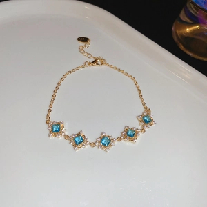 Detailed macro view of gold bracelet featuring square blue zircons with crystal halos