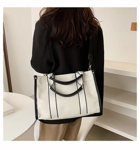 Detail of a large canvas tote bag with black leather trim worn over the shoulder