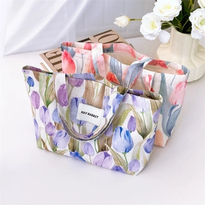 Close-up of canvas tote bags with tulip floral patterns and branding on a desk