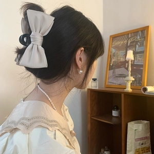 Detail of cream bow hair claw clip styled with elegant pearl jewelry and autumn outfit