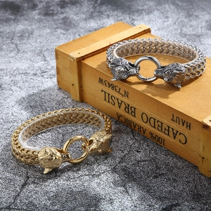 Close-up of gold and silver wolf head bracelets on a rustic wooden decorative box