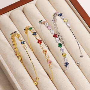 Close-up of gold and silver rainbow zircon open bangles on a beige velvet tray