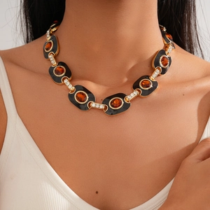 Détail de collier doré avec maillons ovales noirs, pierres ambrées et cristaux scintillants