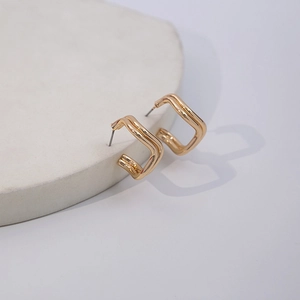 Macro detail of gold geometric double-layered square stud earrings on stone