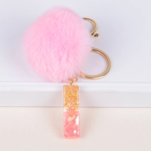 Close-up of pink fluffy pompom keychain with resin gold foil letter pendant detail