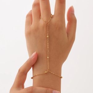 Detail of a gold double-layer hand chain with round beads and finger ring on a female model