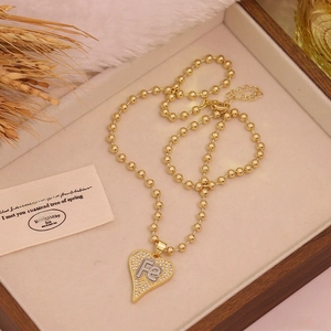 Two-tone heart pendant necklace with zircon pavé and FE initial on wooden box