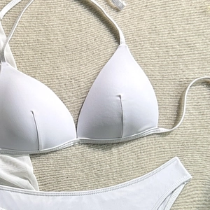 Flat lay of a white three-piece bikini set and sheer mesh skirt on a woven mat