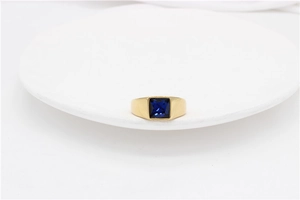Macro shot of a gold-plated titanium ring featuring a square blue gemstone on a white base