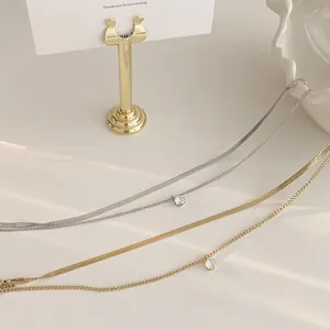 Detail of layered gold and silver snake chains with a single zircon pendant