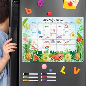 Close-up of magnetic monthly planner with fruit patterns and colorful pens on grey fridge