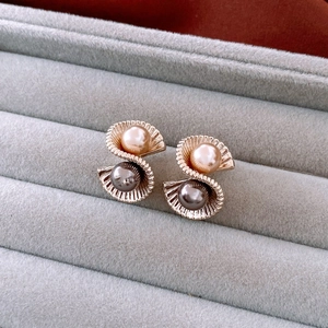 Detail view of gold shell-shaped earrings with champagne and black pearls on velvet