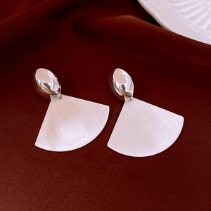 Macro detail of silver geometric fan earrings showing brushed metal texture on velvet