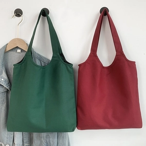 Close-up of forest green and burgundy canvas tote bags hanging against a white wall