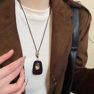Detail of tiger eye stone pendant necklace on brown suede blazer and white sweater