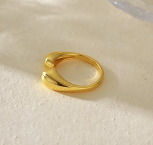 Macro shot of gold double teardrop open ring on a textured cream paper background