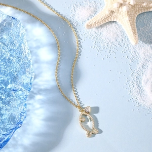 Detail shot of a golden fish-shaped necklace pendant with zircon inlays and sea stars